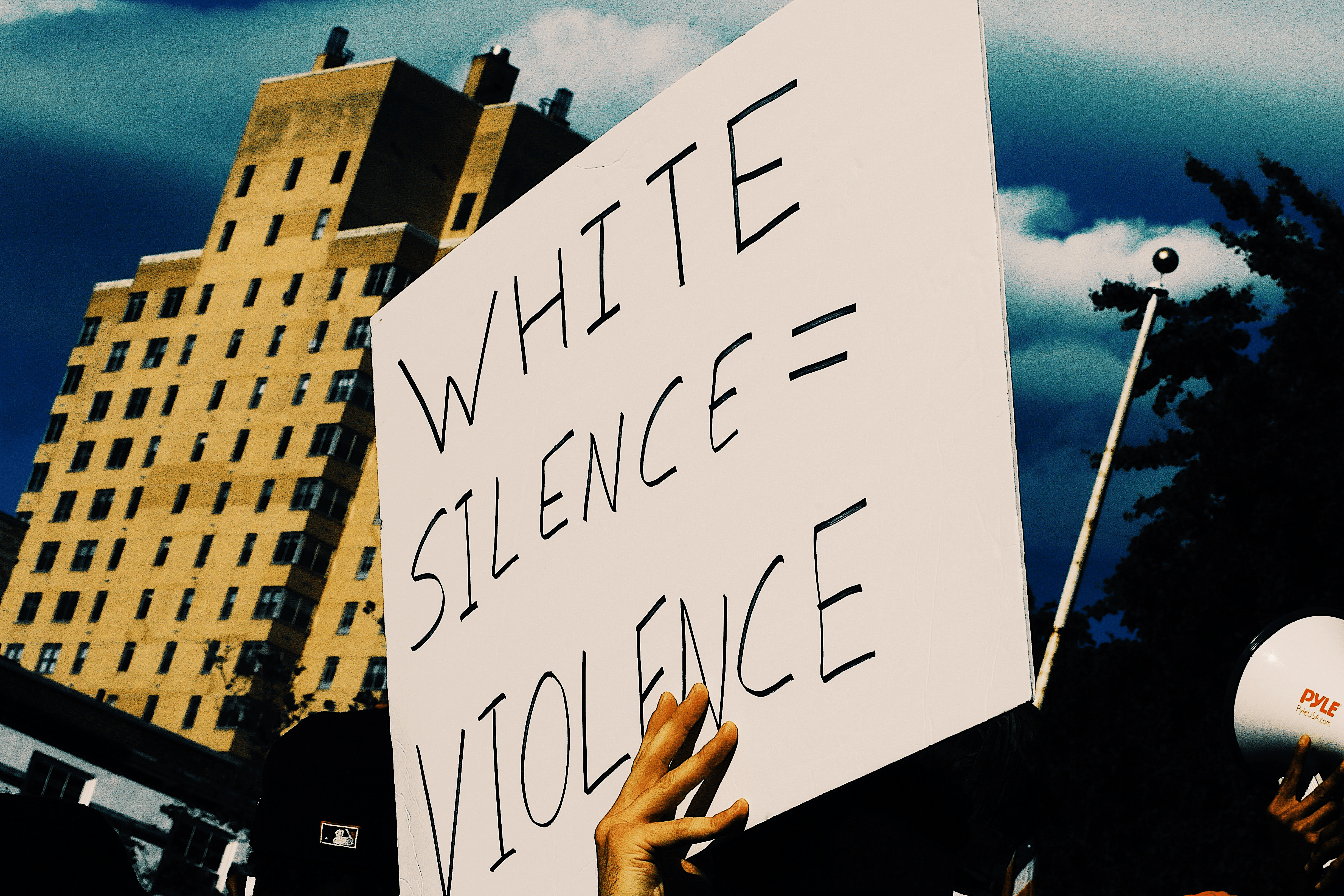 White Silence=Violence’ by Domo, Unsplashed Ltd, 2021 A protest sign being held up by people in New York stating  White Silence=Violence 